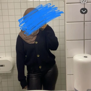 Svart stickad kofta med stora knappar - Säljer en svart stickad kofta med stora, kontrasterande knappar framtill. Koftan har en avslappnad passform och långa ärmar, perfekt att slänga på sig när det är kyligt. Enkel och stilren design som funkar till många outfits.