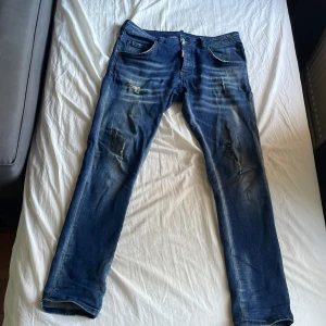 Blåa Dsquared2 jeans  - Säljer ett par blå Dsquared2 jeans. Jeansen har snygga slitningar och blekta partier framtill. Märkespatch bak i midjan och detaljerade sömmar. Dem är ganska använda men är inte i dåligt skick. 