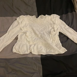 Vit blus med volang från Kappahl - Säljer en söt vit blus från Kappahl i storlek 152. Blusen har långa ärmar, volangdetaljer vid axlar och nederkant samt en lätt struktur i tyget. Perfekt för dig som gillar romantisk och stilren look.