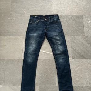 Slim Glenn blå jeans 28/30 - Mörkblå jeans från Jack & Jones i modellen Slim Glenn. Jeansen har klassisk femficksdesign, smal passform och snygga slitningar framtill. Tillverkade i stretchig denim för extra komfort och rörelsefrihet.