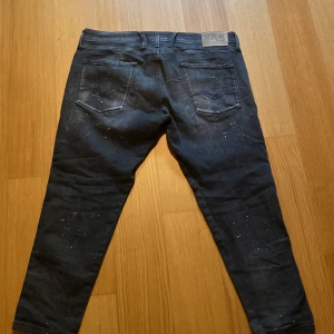 Replay svarta jeans med stänkdetaljer - Säljer ett par svarta Replay jeans med coola vita stänkdetaljer. Jeansen har klassisk femficksdesign, normal passform och snygga slitningar. Materialet är jeans och de har en mörk tvätt som ger en schysst look.