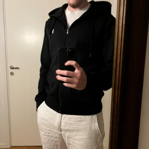 Svart hoodie från Ralph Lauren - Svart Ralph Lauren zip hoodie som är nästan som ny då den knappt är använd och är därför i mycket bra skick! Storleken är S, men skulle nästan säga att den passar M med, personen på bilden är 182