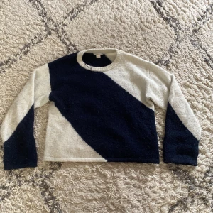 Randig stickad tröja i svart och vit - Snygg stickad tröja med breda diagonala ränder i svart och vitt. Tröjan har rund halsringning och långa ärmar, perfekt för att hålla värmen under kyliga dagar. Mjuk och skön känsla, passar till jeans eller kjol.