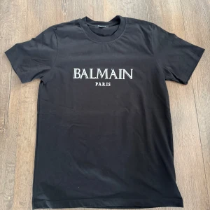 Svart Balmain Paris t-shirt - Snygg svart t-shirt från Balmain Paris med klassisk logga tryckt framtill. T-shirten är i 100% bomull och har rund halsringning och korta ärmar. Perfekt för dig som gillar stilrena och exklusiva plagg med streetkänsla.