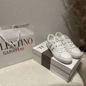 Valentino Rockstud vita sneakers - Snygga vita Valentino Garavani Rockstud sneakers i skinn med silverfärgade nitar och klassisk snörning. Skorna har en platt sula och coola detaljer längs sidorna och hälen. Perfekta för dig som vill sticka ut med en lyxig och edgy stil.
