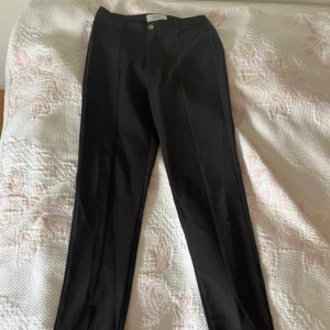 Svarta kostymbyxor från Moves - Svarta kostymbyxor från Moves i storlek 34. Byxorna har raka ben, pressveck och diskreta fickor bak. Klassisk design med knapp och dragkedja framtill. Perfekta för en clean och stilren look.