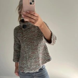 Stickad kofta från Paul Costelloe - Säljer en stickad kofta från Paul Costelloe i grå, beige och orange toner. Koftan har ett grovt mönster, stor krage med dekorativ knapp och trekvartsärmar. Perfekt för lager-på-lager under höst och vinter.