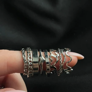 Set med 9 silverfärgade ringar - Säljer ett set med 9 coola ringar i silverfärg. Mixen innehåller både släta och vågiga former, samt ringar med kedjedetaljer och twistad design. Perfekt för dig som gillar att stacka och skapa din egen vibe. Alla ringar är i metall och har olika mönster och former.