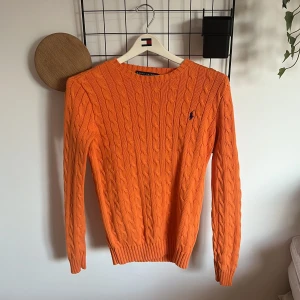 Orange stickad tröja från Ralph Lauren - Orange stickad tröja från Ralph Lauren med klassisk blå broderad logga på bröstet. Tröjan har rund halsringning, ribbade muddar och är långärmad. Skickar den innom 24-48h om tid finns! 