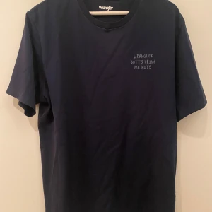 Mörkblå Wrangler t-shirt med brodyr - Mörkblå t-shirt från Wrangler i bomull med broderad text 'Wrangler butts drive me nuts' på bröstet. Klassisk rund hals och korta ärmar. Perfekt för dig som gillar statement-plagg och enkel stil. Watch the mistake!!