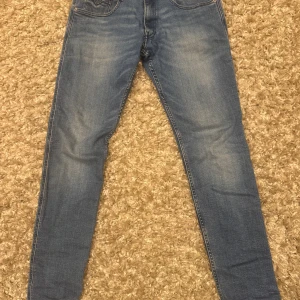 Blå slim anbass från Replay - Säljer ett par blå skinny jeans från Replay med klassisk femficksdesign och snygga slitningar. Jeansen har normalhög midja och är tillverkade i stretchigt denim för en bekväm passform. Perfekta för dig som gillar en smal siluett och stilren look.
