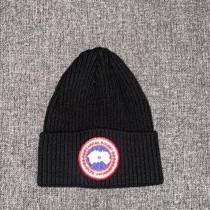 Svart ribbad mössa Canada Goose - Svart ribbstickad mössa från Canada Goose med klassisk rund logotyp-patch framtill i rött. 