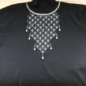 Svart polotröja med pärldetaljer - Svart polotröja med lång ärm och snygga pärldetaljer i ett geometriskt mönster framtill. Tröjan har hög krage och är gjord i ett mjukt stickat material. Perfekt för dig som gillar att sticka ut med coola detaljer och elegant vibe.