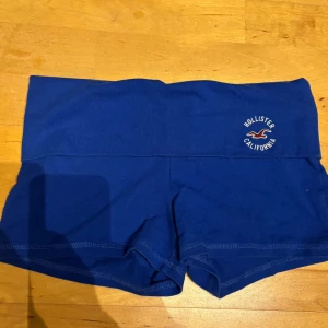 Blåa högmidjade shorts från Hollister - Snygga blåa högmidjade shorts från Hollister med broderad logga framtill. Mjukt och stretchigt material som sitter skönt på kroppen. Perfekta för en chill dag eller när du vill ha något bekvämt och stilrent.