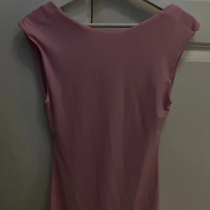 Rosa ärmlös klänning med drapering - Säljer en stilren rosa klänning med mjuk drapering över höften. Klänningen är ärmlös och har en enkel, elegant design med rundad halsringning. Materialet känns slätt och följsamt mot kroppen, perfekt för dig som gillar minimalistisk stil.