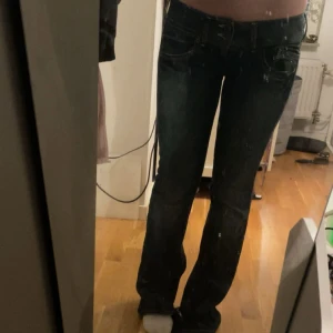 Blå bootcut jeans  - Snygga blå jeans från tommy hilfiger med bootcut. Jeansen har slitningar. Har även sytt om dem lågmidjade vilken man ser på bild 2 och klippt dem längst ner för att få dem mer utsvängda, finns även en blekningsfläck längst ner på högra benet. Midja 41x2  cm, innerben 83cm, lår 26x2 cm 