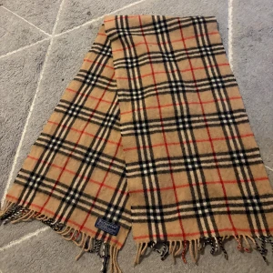 Burberry scarf  - Klassisk halsduk från Burberrys i beige, svart, rött och vitt med ikoniskt rutmönster. Gjord i en lyxig mix av 50% kashmir och 50% ull. Mjuka fransar i ändarna och snygg vintage-vibe. Perfekt accessoar för att lyfta din outfit.