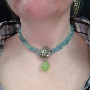 Halsband med blågröna stenar - Snyggt chocker halsband med blågröna stenar. Detaljer med vacker hjärtformad knapp och kulhänge. Ca 38 cm långt