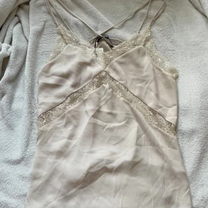 Champagnefärgad spetstopp - Champagnefärgad spetstopp från Bik Bok med tunna axelband som korsas i ryggen. Klänningen har vackra spetsdetaljer längs halsringningen och midjan. Små fläckar på sista bilden som ni ser. Storlek L. Nypris 300 kr och inte använd. säljer för 170 kr🙏💕