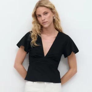 Svart omlottopp med knyt i midjan - Svart omlottopp från gina med djup v-ringning och långa ärmar. Toppen har knytband i midjan som ger en snygg siluett och är tillverkad i ett mjukt bomullsliknande material. Perfekt att styla med jeans eller kjol för en trendig look. OBS! Inte samma som bilden!