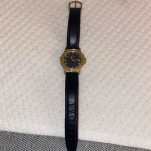 Svart skinnbälte från Jaguar - Snyggt svart bälte i äkta skinn från Jaguar med klassisk form och guldfärgat spänne. Bältet har en stilren look och passar perfekt till jeans eller kostymbyxor. Märket syns tydligt på insidan av bältet och ger en exklusiv känsla.det är en ska som har låsnat i klockan fast det går att fixa fast man måste ta den till en Klock-butik och den behöver ett nyt battery 