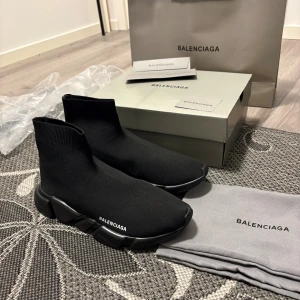 Balenciaga Speed Trainer svarta sneakers - Svarta Balenciaga Speed Trainer sneakers med stickad ovandel i syntet och chunky platt sula. Minimalistisk design med Balenciaga-logga på sidan och elastisk strumpkonstruktion som sitter tight runt foten. Perfekt för dig som gillar streetwear och lyxiga detaljer.