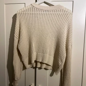 Beige ribbad stickad tröja - Säljer en beige stickad tröja med ribbad struktur och avslappnad passform. Tröjan har lång ärm och lite längre baktill för en snygg och chill look. Perfekt att slänga på sig när det är kyligt ute.