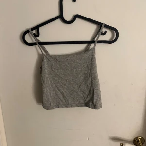 Grå croppad linnetopp med smala axelband - Säljer en enkel och stilren grå croppad linnetopp med smala axelband. Toppen har en rak och kort passform som är perfekt för varma dagar. Materialet känns mjukt och lätt mot huden, och färgen är neutral vilket gör den lätt att matcha med andra plagg.