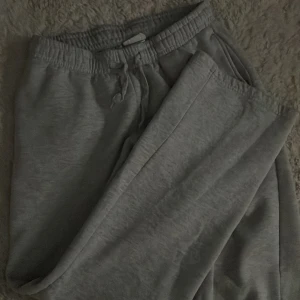 Grå mjukisbyxor från Gina Tricot - Snygga grå mjukisbyxor från Gina Tricot med rak passform och elastisk midja med snörning. Tillverkade i mjukt bomullsmaterial som är skönt mot huden. Perfekta för chill dagar och har en enkel, stilren look.