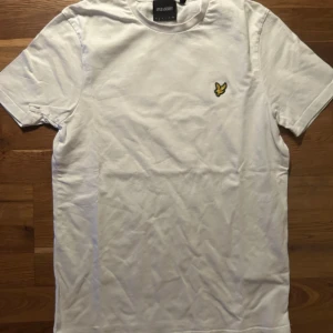 Vit t-shirt från Lyle & Scott - Vit t-shirt från Lyle & Scott med klassisk rund hals och korta ärmar. På bröstet sitter den ikoniska broderade gula fågeln. T-shirten är gjord i mjuk bomull och har en clean, stilren look som funkar till jeans eller shorts. Pris går att diskutera vid snabb affär!