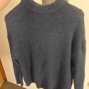 Mörkblå stickad polotröja - Mysig mörkblå stickad polotröja med hög krage och långärmad design. Perfekt för kyliga dagar och enkel att matcha med jeans eller kjol. Materialet är mjukt och ger en avslappnad vibe. Snygg att ha lager på lager under jacka.