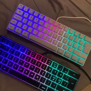 RGB Mekaniskt Tangentbord (vit och svart) - Två kompakta mekaniska tangentbord med nordisk layout och RGB-belysning. Ett vitt och ett svart, båda med färgglad bakgrundsbelysning. Tangenter och hölje i mycket gott skick, inga synliga repor eller skador. Perfekt för gaming eller arbete.