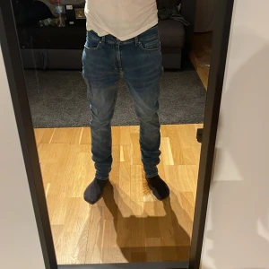 Blå jeans från dressman - Säljer ett par klassiska blå Levi's 511 jeans med normal passform och raka ben. Jeansen har fem fickor, bälteshällor och snygga slitningar på framsidan för en cool look. Perfekt för dig som gillar stilrena och tidlösa jeans.