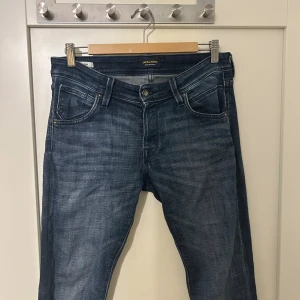 Blå jeans från Jack & Jones - Snygga blå jeans från Jack & Jones med klassisk femficksdesign och diskret slitning. Jeansen har normal passform och raka ben, tillverkade i mjukt bomullstyg med en lätt tvättad look. Perfekta för en avslappnad stil.