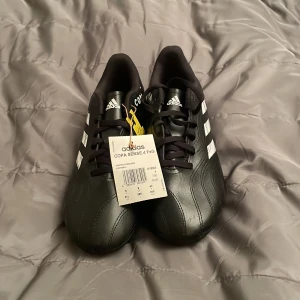 Adidas Copa Sense.4 Svarta Fotbollsskor - Säljer ett par svarta Adidas Copa Sense.4 fotbollsskor i storlek 42 med vita detaljer och klassiska tre ränder på sidan. Skorna har snörning, rund tå och platt sula med dobbar för gräsplan. Materialet är syntet och skinn för bästa komfort och grepp på planen.