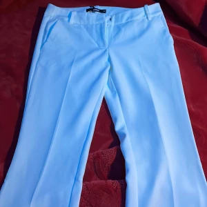 Vita kostymbyxor från Bik Bok, stl 34 - Snygga vita kostymbyxor från Bik Bok i storlek 34. Byxorna har raka ben, hällor för bälte och diskreta fickor fram. Perfekta för en clean och stilren look. Materialet är slätt och känns lyxigt, med klassisk dragkedja och knapp framtill. Jätte lågmidjade kostymbyxor. Aldrig använda för att de har varit för långa för mig. 