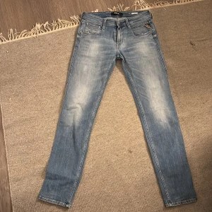 Replay Anbass ljusblå jeans - Säljer ett par Replay Anbass jeans i ljusblå tvätt med snygga slitningar och klassiska fem fickor. Jeansen har raka ben, normal passform och detaljer som Replay-logga på bakfickan och läderpatch i midjan. Perfekt för dig som gillar stilrena och bekväma jeans. Midjemått rakt över är 40 , och innrebenslängden är 81 cm. Pris kan diskuteras 