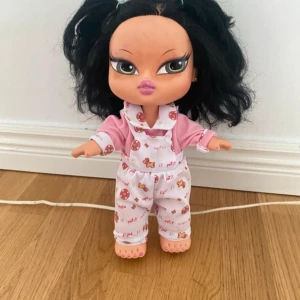 Lila och vit randig dockklänning - Söt kort klänning till docka i lila och vitt med breda horisontella ränder. Klänningen är ärmlös och har en enkel, avslappnad passform. Perfekt för att ge dockan en färgglad och lekfull look.