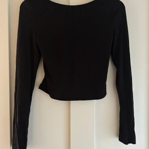 Svart topp med öppen rygg från SHEIN - Svart långärmad topp från SHEIN i storlek M. Toppen har en snygg öppen rygg och enkel, stilren design. Materialet är mjukt och stretchigt. Perfekt för dig som gillar minimalistisk stil och vill ha något som sticker ut med den öppna ryggen.