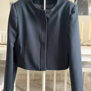 Mörkblå croppad kavaj från Zara - Snygg mörkblå croppad kavaj från Zara med stilren design och rund halsringning. Jackan har dold dragkedja framtill och raka långärmade ärmar. Materialet är slätt och känns lyxigt, perfekt för dig som gillar minimalistisk stil.