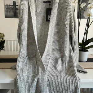 Grå stickad kofta med huva FB Sister - Säljer en grå, stickad kofta från FB Sister i storlek XL. Koftan har huva, två stora fickor fram och är långärmad. Ribbad struktur och loose passform gör den extra chill. Perfekt att slänga på sig när det är lite kyligt ute.