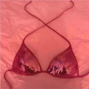 Rosa paljett bikini med snörning - Säljer en snygg rosa bikiniöverdel med paljetter som glittrar i ljuset. Triangelformade kupor och tunna snören som knyts i nacken och ryggen. Perfekt för dig som vill sticka ut på stranden eller vid poolen. Trendig och ungdomlig vibe!