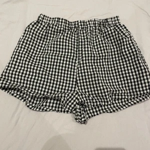 Svartvita rutiga shorts med resår - Snygga svartvita shorts med rutigt mönster och bekväm resår i midjan. De har en loose passform och är perfekta för varma dagar. Tillverkade i ett lätt och mjukt material som känns skönt mot huden.