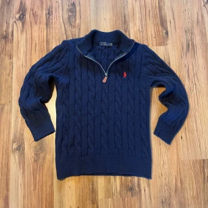 Marinblå kabelstickad tröja Polo Ralph Lauren - Snygg marinblå kabelstickad tröja från Polo Ralph Lauren i storlek M/175 men de står XL. Tröjan har half zip med krage, långärmad design och röd broderad logga på bröstet. Tillverkad i 100% bomull och har ribbade muddar vid ärmslut och nederkant. Inga defekter eller skador.                                                Pris går att diskutera 🫡