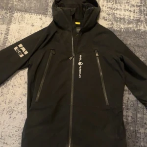 Svart vindjacka Sail Racing M - Svart vindjacka från Sail Racing, både vattentät och vindtät. Storlek M men är lite stor i storleken så kan passs också i storleken L. Knappast använd 