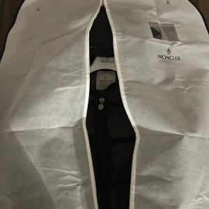 Svart pufferjacka från Moncler - Säljer en svart, glansig pufferjacka från Moncler med huva och klassisk logga på ärmen. Jackan har dragkedja framtill och breda, quiltade sektioner som ger en riktigt fet look. Perfekt för dig som vill ha en varm och snygg jacka med street-vibe.Köpt från stockx