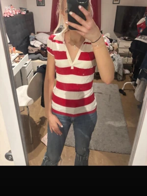 Randig röd och vit t-shirt Lindex - Säljer en kortärmad t-shirt från Lindex i storlek XS. T-shirten har breda röda och vita ränder, v-ringning med liten knappdetalj och är i mjuk bomull. Perfekt till jeans för en chill look.