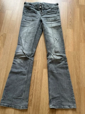 Grå bootcut jeans med fickor från och bak - Säljer ett par grå jeans med bootcut passform och fickor fram. Jeansen har dubbla knappar i midjan och klassiska bakfickor. Materialet är mjukt jeans och färgen är snyggt tvättad grå. 