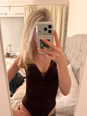 Vinröd spetsdetaljerad body - Säljer en vinröd body med v-ringad hals och fina spetsdetaljer längs urringningen. Västen är figurnära och har en elegant, feminin look. Perfekt att styla med jeans eller kjol för en trendig outfit.