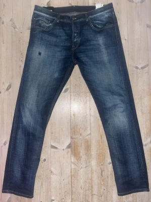 Dondup jeans - Säljer ett par snygga blå jeans från Dondup, tillverkade i Italien. Jeansen har en klassisk femficksmodell, orange sömmar och en cool tvättad look med slitningar. Materialet är jeans och passformen är rak med normal midja. Perfekta för dig som söker något mindre slimmat jämfört med George. Tveka inte om du har fler frågor!